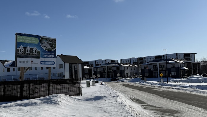 Un quartier résidentiel en hiver avec une affiche promotionnelle indiquant son développement en cours.