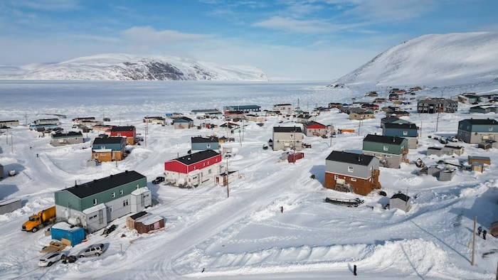Le village enneigé avec plusieurs maisons bicolores est réparti de part et d'autre d'une petite route.