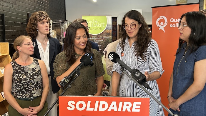 Ruba Ghazal se tient derrière un lutrin avec des employés et des membres de son parti. Des micros sont pointés vers elle, car elle est en conférence de presse.