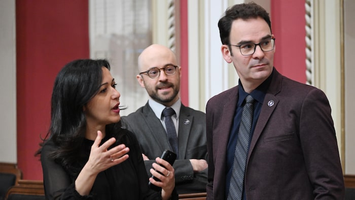 Ruba Ghazal s'entretient avec le député Etienne Grandmont sous le regard du député Sol Zanetti, à l'occasion d'une pause à l'Assemblée législative, à Québec.