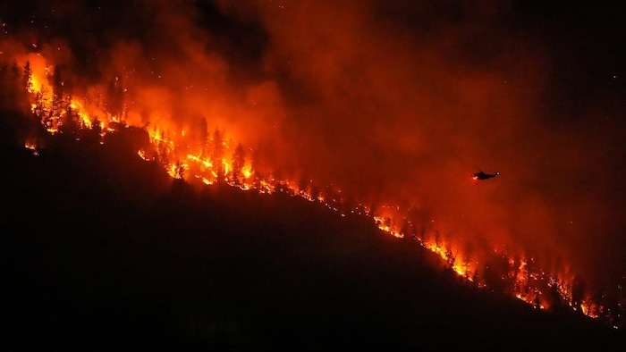 La nuit, un hélicoptère se prépare à arroser un brasier qui ravage une forêt au sommet d'une crête.