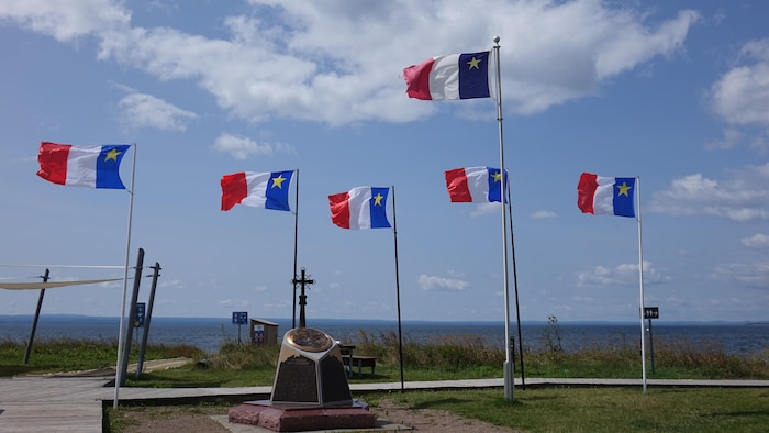 Un monument devant le fleuve. Des drapeaux acadiens flottent au-dessus.