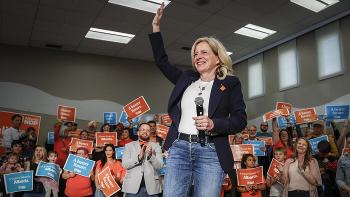 Rachel Notley salue une foule de partisans tenant des affiches de son parti.