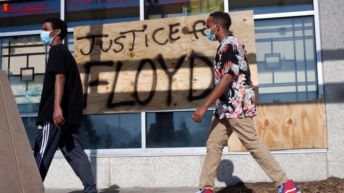 Deux jeunes Afro-Américains portant un masque et marchant devant un graffiti disant « Justice pour Floyd ».