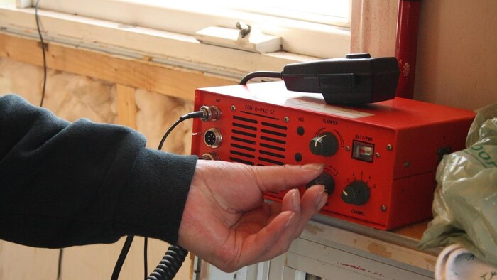 Un main manipule un bouton rotatif sur une petite radio rectangulaire.