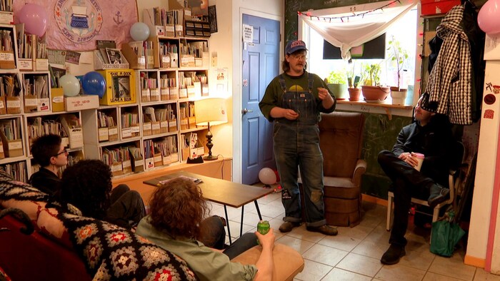Un espace salon aux allures alternatives, avec cinq personnes discutant. Le mur est rempli de zines.
