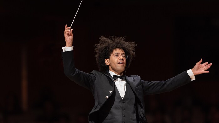 Le chef dirige l'orchestre, baguette en l'air.