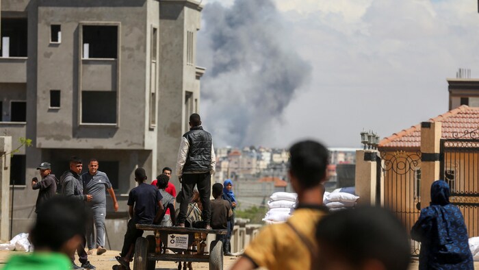 Des Palestiniens regardent une colonne de fumée noire au loin.