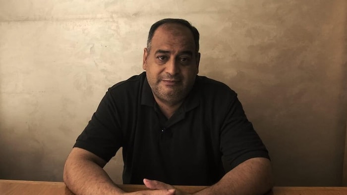 Un homme assis face à la caméra.