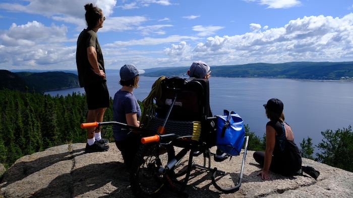 Quatre personnes, dont une en fauteuil roulant adapté, observent la baie des Ha! Ha! du haut du sentier Eucher, à La Baie.