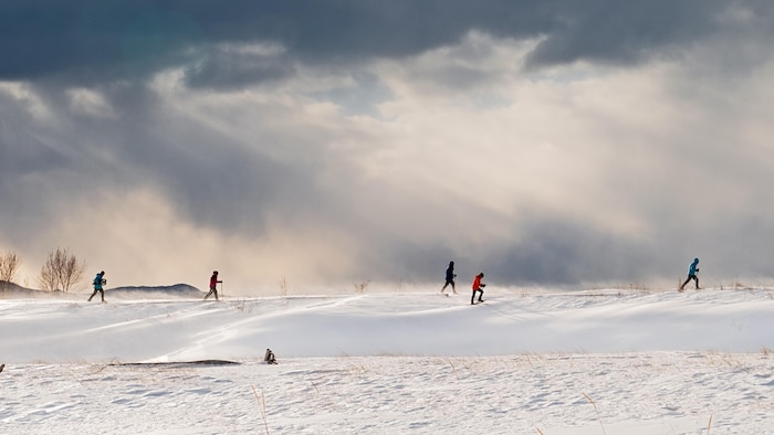 Des gens en raquette dans la neige, sous un ciel menaçant et lumineux à la fois.