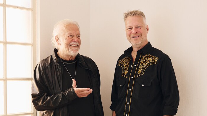 Le père et le fils, deux musiciens, sourient l'un à côté de l'autre. 