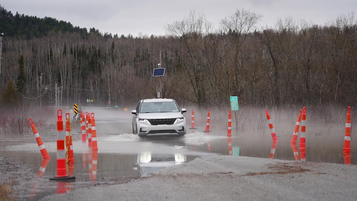 Un véhicule roule sur une route en partie inondée.