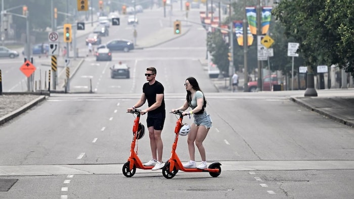 Deux personnes utilisant des trottinettes électriques en pleine circulation.
