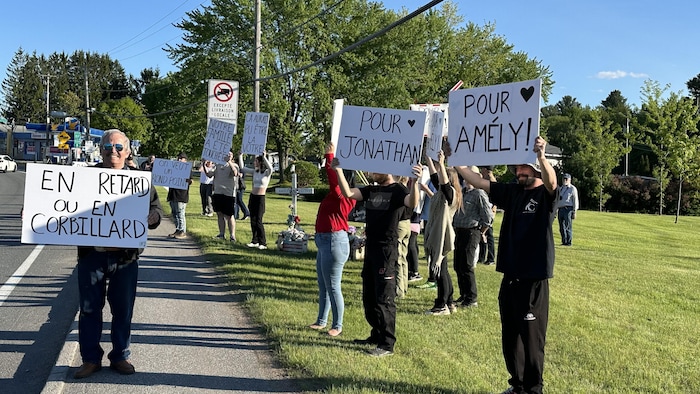 Des personnes tiennent des pancartes près d'une route.