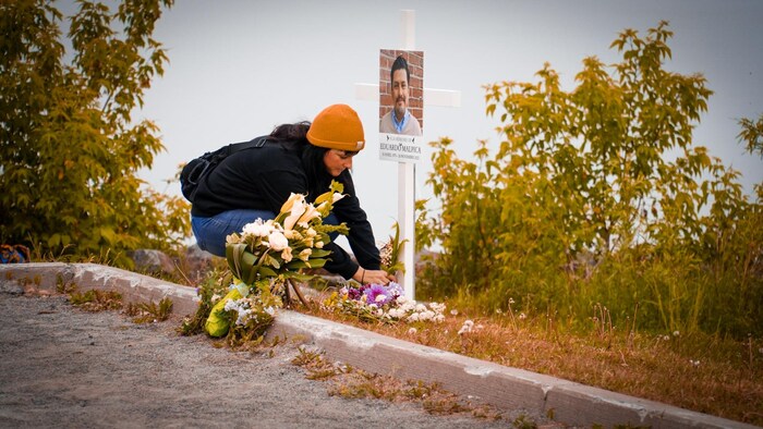 Une femme dépose des fleurs au pied de la croix.