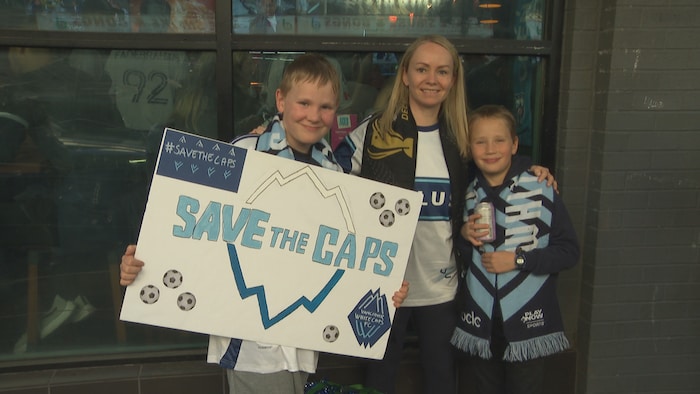 Une adulte et deux enfants avec une pancarte « save the caps ».