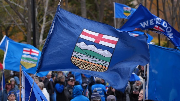 Un drapeau albertain avec des militants habillés en bleu en arrière-plan.