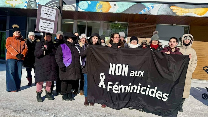 Des femmes tiennent une bannière et une pancarte dénonçant les féminicides.