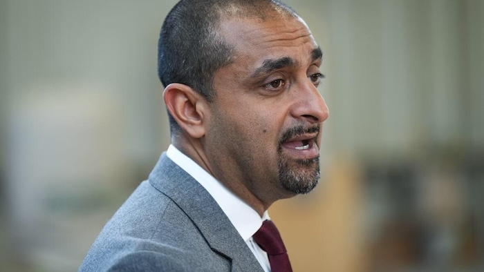 Ravi Kahlon parle. Il porte un veston-cravate.