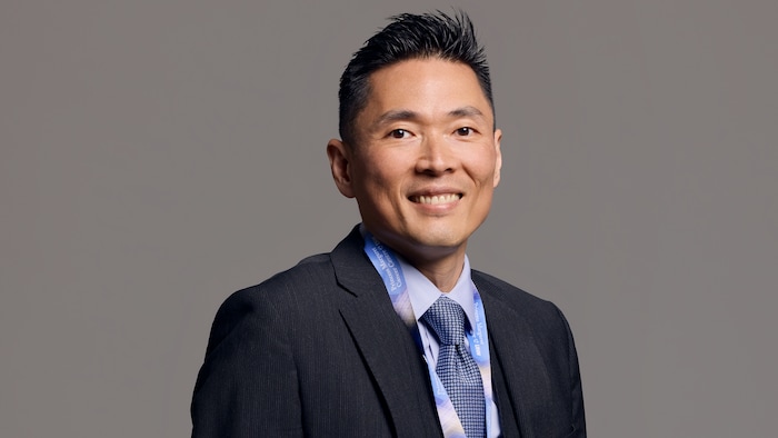 Dr Raymond Kim est debout et sourit à la caméra. 