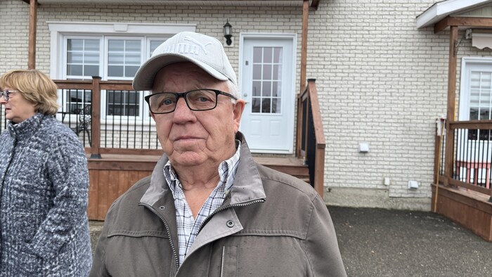 Raymond Pitre pose pour une photo à l'extérieur, devant un immeuble.