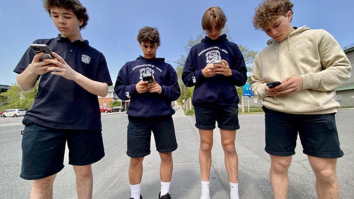 quatre adolescents sont debout, visage rivé sur l'écran de leur téléphone cellulaire