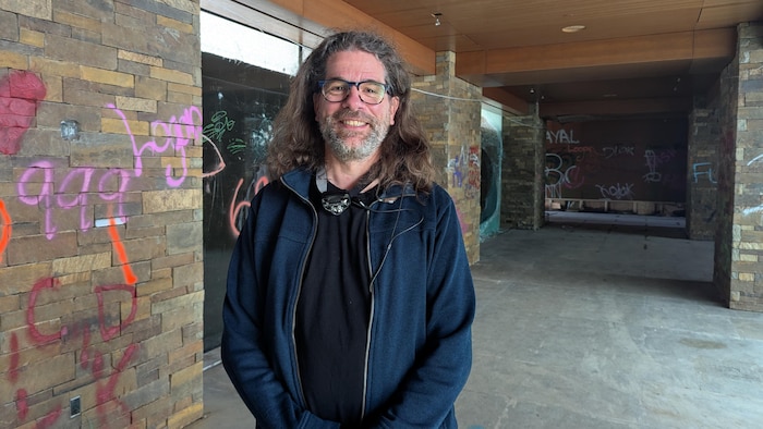 Un homme est debout dans un corridor du manoir qui comporte plusieurs graffitis.