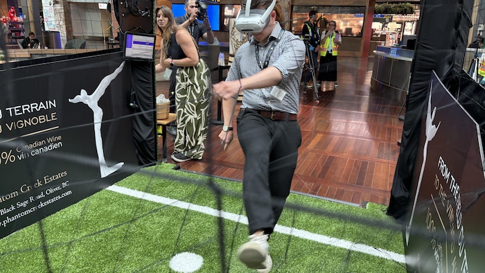 Un homme donne un coup de pied dans un petit enclos de réalité virtuelle, sur une fausse pelouse de soccer.