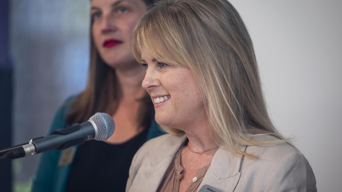 Rebecca Bligh est devant un micro. Elle sourit en regardant droit devant elle.