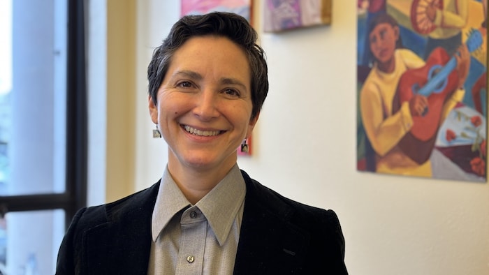 Une femme sourit dans un bureau avec des peintures colorées en arrière-plan. 