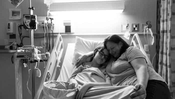 Une jeune fille dans un lit d'hôpital et une adulte qui l'entrelace.