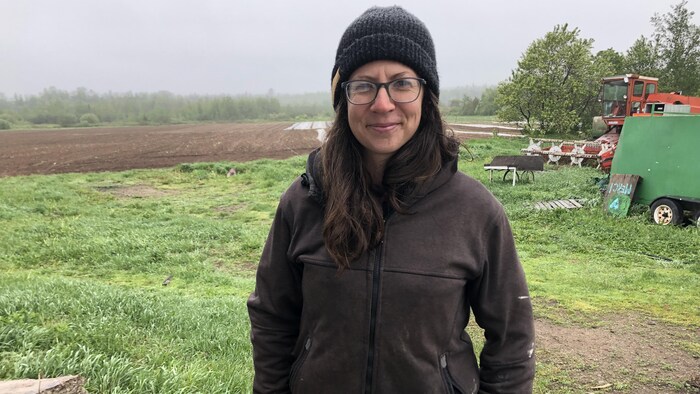 Une femme sourit à la caméra, un champ derrière elle.
