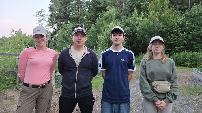 Quatre personnes posent debout côte à côte devan une forêt.