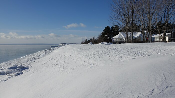 Entre une habitation et la mer, la recharge de plage forme une butte de plusieurs mètres couverte de neige.