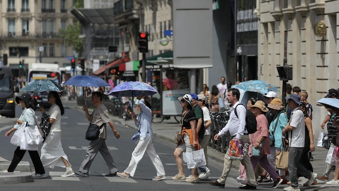 Des gens se protègent du soleil sous des parasols à Paris le 23 juin 2026.