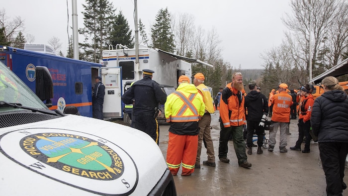 Par temps gris et pluvieux, des personnes circulent autour d'un camion de la GRC et d'un camion identifié par les mots «Pictou Country Search and Rescue».