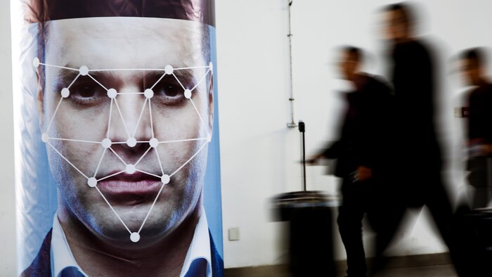 Des personnes passent devant une affiche d’un logiciel de reconnaissance faciale.