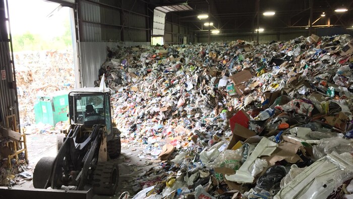Une chargeuse déplace des montagnes de matières recyclables dans un hangar.