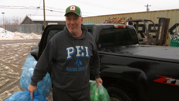 Un homme souriant sort trois sacs d'un compartiment d'une camionnette.