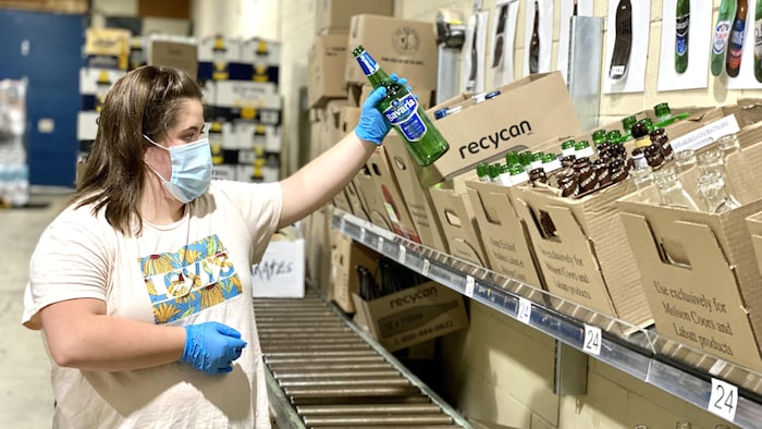 Une personne dépose une bouteille de verre dans une caisse de carton. 