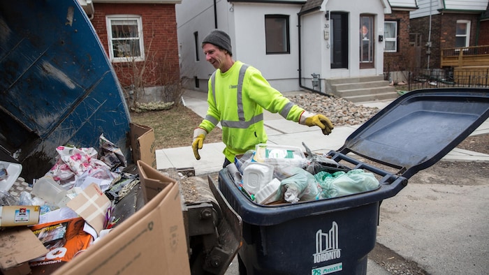 Un employé municipal de Toronto approche un bac de recyclage du camion lors de la collecte.
