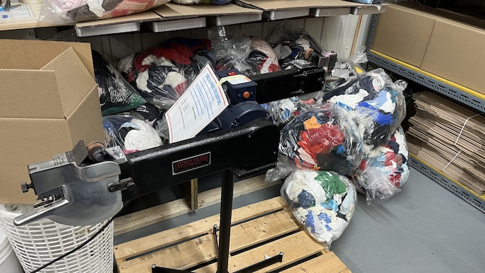 Des sacs transparents remplis de textiles sont posés par terre dans un entrepôt.