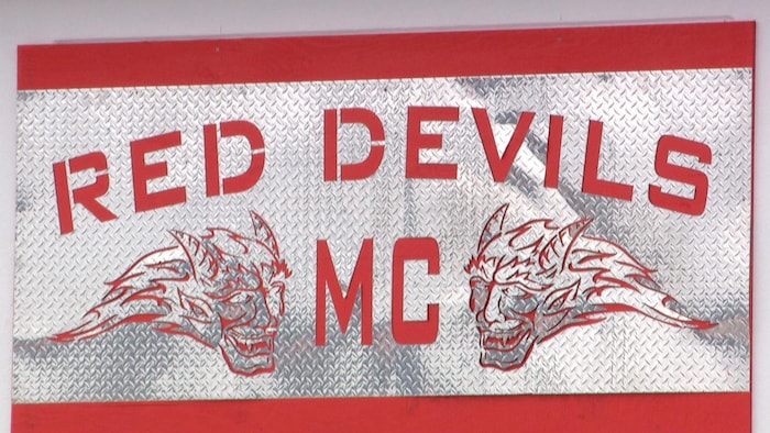 Une enseigne de métal, avec des contours rouges, sur laquelle ont peut lire les mots Red Devils MC. 