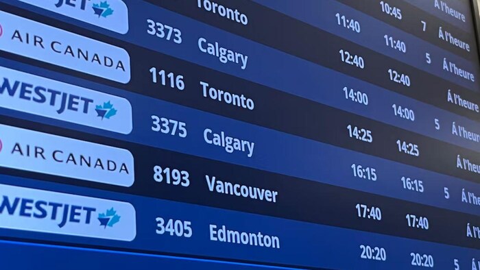 Un gros plan sur l'écran bleu des départs de l'aéroport international de Regina (YQR) affiche les numéros de vol, les horaires et les destinations canadiennes.