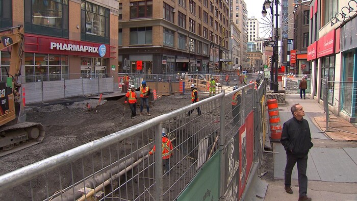 Un homme se promène en bordure du chantier tout en regardant les façades des magasins.