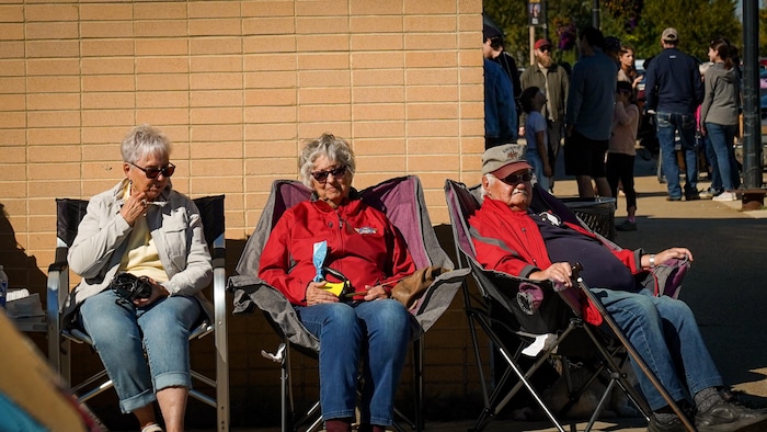 Trois personnes âgées profitent du soleil dans un festival familial à Grimshaw, en Alberta.