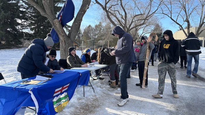Des personnes en train de faire la file devant des tables avec des drapeaux albertains, dans un parc à Edmonton, en janvier 2026.
