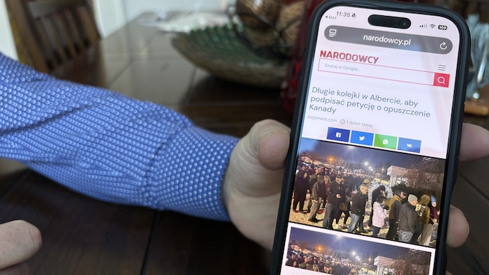 La main d'une personne montre un téléphone sur lequel est affiché un article en polonais en janvier 2026 en Alberta.
