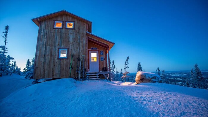 Vue extérieur d'un chalet dans un décor hivernal à la tombée du jour.